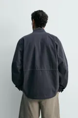 Cazadora regular fit de algodón color gris oscuro con efecto lavado, cuello subido, manga larga y cierre frontal con cremallera oculta por solapa con botones a presión. Cuenta con cuatro bolsillos frontales de plastrón con solapa y cintura ajustable con cordón interior.