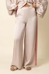 Pantalón palazzo de satén color beige con franja vertical rosada en los laterales.