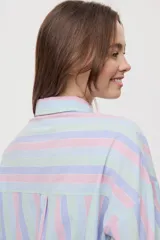 Camisa oversize de manga larga con estampado de rayas verticales en tonos rosado, celeste y verde menta. Cuenta con cuello camisero, cierre frontal con botones y un bolsillo aplicado en el pecho.