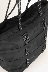 Bolso tipo tote color verde militar con múltiples correas horizontales y verticales. Tiene doble asa de soga trenzada y cierre superior con cremallera.