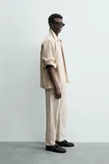 Pantalón chino de corte relajado, color beige claro, con textura de rayas verticales sutiles. Presenta cintura ajustable con cordón interior, bolsillos delanteros y bolsillos traseros de vivo.