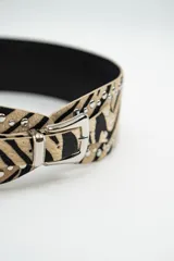 Cinturón de cuero con estampado animal print de cebra, decorado con tachas metálicas plateadas a lo largo de los bordes y hebilla metálica plateada.