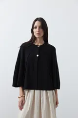 Saco tipo capa de punto color negro, con silueta fluida, corte amplio y cierre frontal con dos botones dorados.