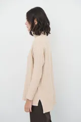 Polera de tejido de punto acanalado en color beige, con cuello alto, manga larga y diseño de corte recto con aberturas laterales en el ruedo.