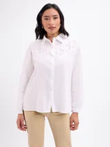 Camisa blanca de algodón, de manga larga, con detalle de tiras cruzadas en el canesú delantero y cierre frontal con botones.