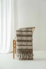 Manta tejida a crochet con diseño a rayas horizontales en tonos crudo y marrón, con flecos en los extremos.