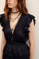 Vestido largo negro de poliéster, con escote en V profundo, mangas sisa con volados en los hombros, cintura elastizada con diseño fruncido y falda larga con capas y volados.