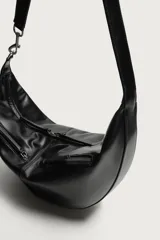 Bolso de hombro de diseño curvo en color negro, con detalle de pespuntes centrales. Cuenta con un compartimento principal con cierre de cremallera y dos bolsillos frontales con cierre. Incluye asa de hombro y bolsillo interior con cierre.