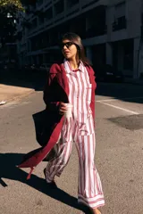 Conjunto de pijama de dos piezas compuesto por una camisa de manga larga con botones frontales y un pantalón de corte holgado, ambos con estampado de rayas verticales en tonos azul y blanco. El pantalón cuenta con un detalle de vivo en color oscuro en el ruedo.