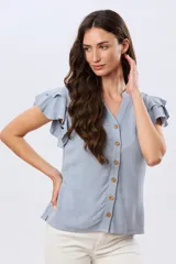 Camisa de lino y viscosa color beige, con cuello mao, escote en V y botones frontales de madera. Presenta mangas cortas con volados delicados.