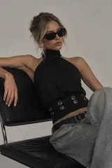 Top halter negro con cuello alto y silueta fluida, con detalle de ojales metálicos en la cintura.