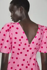 Top rosado con estampado de lunares fucsia, de cuello redondo y mangas cortas abullonadas con pliegues. Cuenta con escote en V en la espalda y cierre con cremallera oculta.