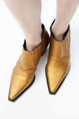 Botines dorados de cuero con punta fina, taco cuadrado bajo y laterales elásticos.