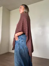 Ruana tejida de algodón con hilo lurex en punto jersey, color azul, con diseño amplio y detalle de etiqueta de cuerina en la parte posterior.