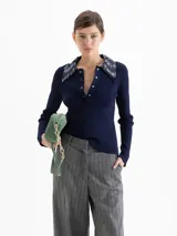 Top de punto acanalado color azul marino, con mangas largas y cuello camisero bordado con lentejuelas al tono. Presenta cierre frontal con broches metálicos.