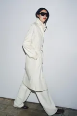 Gabardina oversize color blanco roto, con cuello solapa, manga larga y bolsillos laterales ocultos. Presenta cintura ajustable con cordones a tono y forro interior.