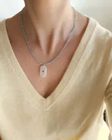 Collar de piedras celestes facetadas en forma de cuentas esféricas, con cierre dorado y un dije colgante rectangular de piedra clara con un detalle circular rojo en el centro.