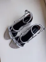 Sandalias plateadas de cuero nobuk, con tiras finas cruzadas en el empeine y tobillo, ajuste de pulsera y taco cuadrado de 7 cm.