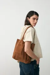 Bolso tipo tote de cuero gamuzado color tostado, con diseño de doble asa y cierre mediante cordón ajustable en la parte superior.