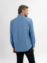 Camisa de jean de manga larga con cuello clásico, cierre frontal con botones y un bolsillo en el pecho.