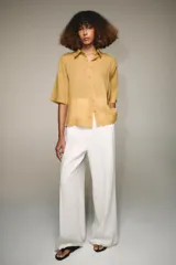 Camisa de color mostaza, con cuello solapa, manga corta y bajo recto. Cierre frontal con botones.