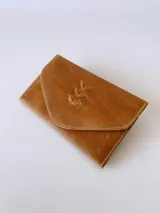 Billetera tipo sobre confeccionada en cuero color camel, con solapa en punta y detalle de costura decorativa en forma de espiga. Cuenta con cierre de broche y monedero externo.