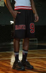 Bermuda deportiva negra de estilo NBA, confeccionada en tejido de punto deportivo. Presenta un elástico en la cintura con franjas rojas y blancas. Estampado frontal con la palabra "RAVERS" y el número "90" en rojo con borde blanco.