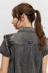 Campera de jean color gris con efecto acid wash, corte clásico y cierre frontal de botones metálicos. Presenta cuello camisero, bolsillos ribeteados y está decorada con apliques de tachas plateadas en el cuello, el canesú frontal, los bordes de la botonera, los bolsillos y el ruedo.