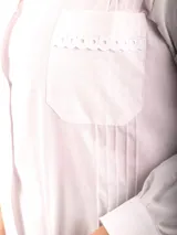 Túnica blanca de dama con cuello camisero, abotonada al frente, con dos bolsillos frontales con detalle de puntilla y pinzas verticales.