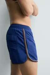Short de baño azul con cintura elástica ajustable con cordón, bolsillos laterales y ribetes en contraste en los bordes.