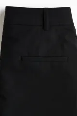 Pantalón recto de color negro con pollera mini superpuesta de corte asimétrico y cierre oculto lateral.