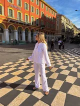 Camisa blanca de broderie con cuello camisero, mangas largas y cierre frontal con botones.