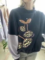 Buzo cropped de algodón color verde militar, con mangas ranglan y diseño estampado en el frente con motivos de besos y moños. Cuenta con elástico holgado en la cintura y los puños.