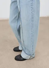 Jeans tiro medio color celeste, de diseño recto y largo, con bajo vuelto, trabillas, cierre de botón y cremallera, estilo cinco bolsillos y detalle de costuras verticales.