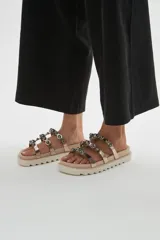 Sandalias chatas de plataforma dentada negra, con múltiples tiras metalizadas decoradas con tachas esféricas brillantes.