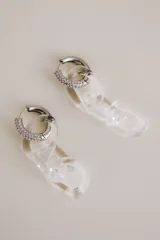 Aros colgantes compuestos por una argolla de plata 925 con incrustaciones de cristales y un dije de cadena de eslabones de vidrio transparente.