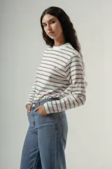 Camiseta de manga larga, cuello redondo, con rayas horizontales marrones sobre fondo blanco. Presenta un pequeño logo bordado en rojo en el pecho.