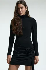 Vestido corto de punto color negro, con cuello alto, mangas largas con hombreras y corte ajustado. Presenta un panel delantero en la cadera con un aplique de rosa y una tira larga lateral.