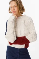 Sweater de punto con diseño de bloques de color en tonos crema y marrón. Presenta cuello redondo, mangas largas y una silueta holgada con detalle de placa metálica decorativa en el lateral.