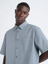 Camisa celeste de manga corta, con cuello clásico, cierre frontal con botones, bolsillo en el pecho con logo bordado de la marca Calvin Klein y corte holgado.