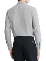 Camisa de vestir gris claro de manga larga, con cuello clásico y cierre de botones. Tiene el logo de Calvin Klein bordado en el pecho.