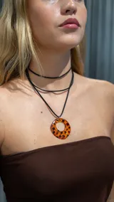 Gargantilla doble de terciopelo negro con dije circular de acrílico color ámbar con manchas negras.