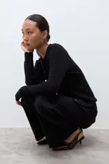 Cardigan negro de punto con textura geométrica, cuello redondo y cierre frontal con botones pequeños. Presenta mangas largas y un diseño ajustado.
