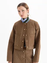 Chaqueta matelaseada color marrón, de corte recto y largo a la cadera, con cuello redondo, cierre frontal con broches dorados y bolsillos plaqué en el delantero.