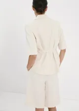 Blazer corto de mezcla de lino en color beige con rayas sutiles, de corte recto, cuello con solapa de muesca, mangas tres cuartos, cierre frontal de un botón y bolsillos con solapa.
