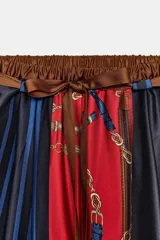 Pantalón de tiro alto con cintura elástica y bolsillos delanteros. Presenta un estampado de cadenas, cinturones y rayas en bloques de color rojo y azul marino. Incluye un cinturón del mismo tejido.