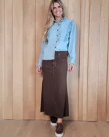 Pollera larga de corte recto y tiro alto, confeccionada en denim color marrón chocolate. Presenta diseño clásico de cinco bolsillos, cierre frontal con botón y costuras reforzadas.