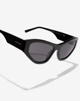 Lentes de sol Hawkers x Tini modelo Code, con armazón de acetato negro y diseño cat-eye. Presentan cristales oscuros y detalles de marca grabados en las patillas.