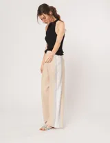 Pantalón palazzo color beige con cintura elastizada y dos franjas verticales en los laterales, una plateada y otra blanca.