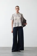 Camisa de manga corta abullonada, con cuello camisero y botones frontales. Presenta un estampado de inspiración barroca en tonos marrón y beige claro.